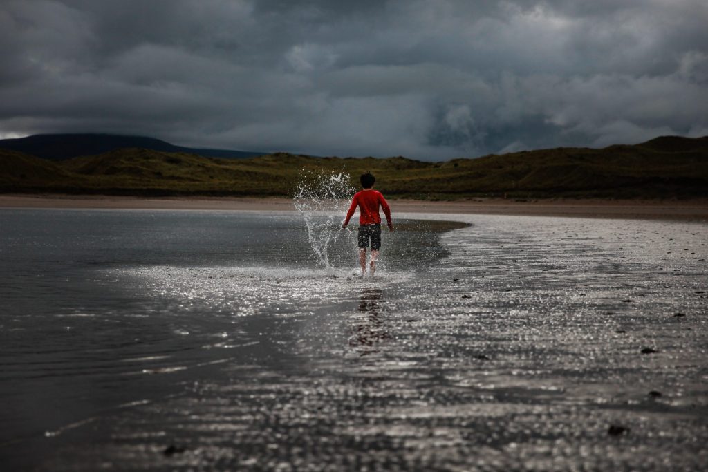 Young boy walking with splashes along the shore line shallow water