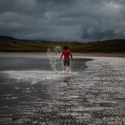 Young boy walking with splashes along the shore line shallow water