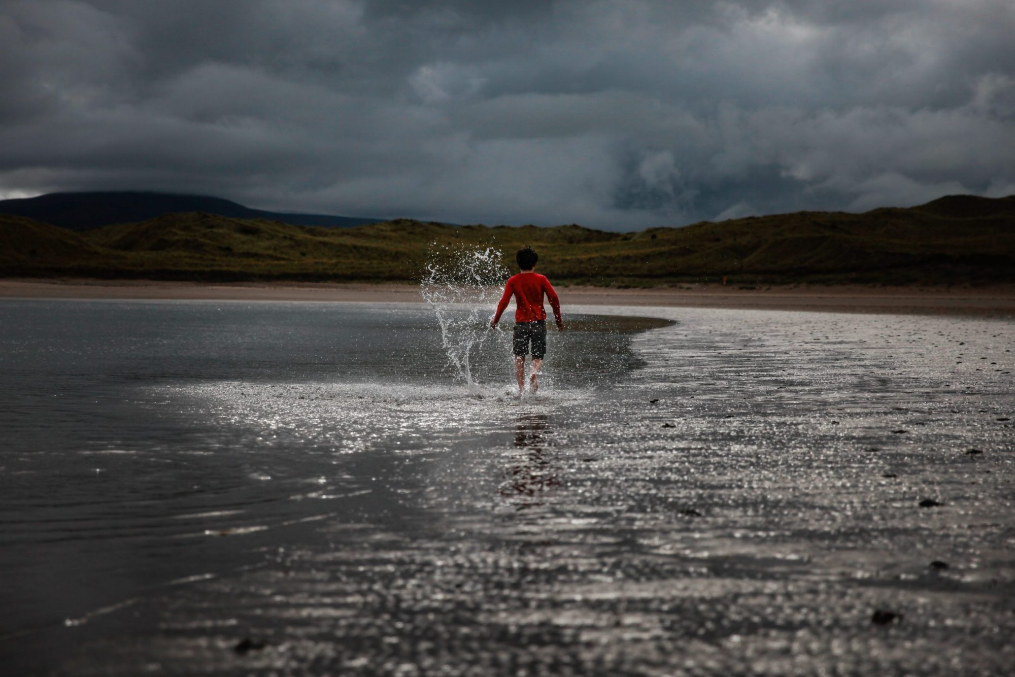 Young boy walking with splashes along the shore line shallow water