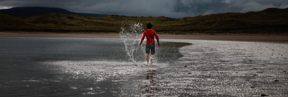 Young boy walking with splashes along the shore line shallow water