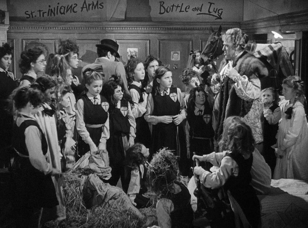 Scene from the film "Belles of St Trinians". Schoolgirls crowded into a room with a horse being lectured to by their headmistress.