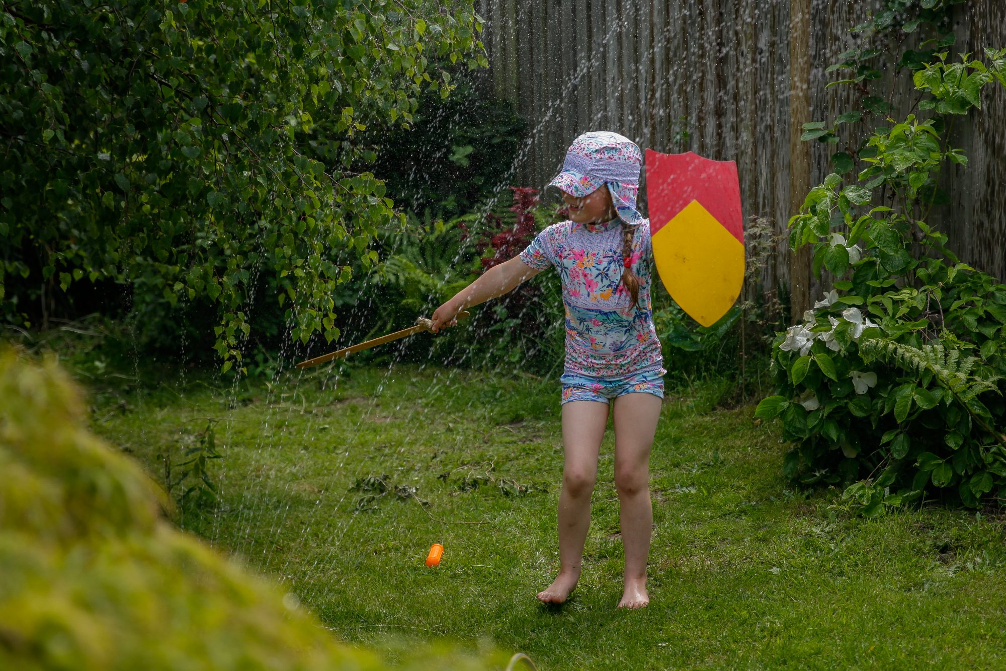 Young girl with decorated shield and sword playing with water sprinkler