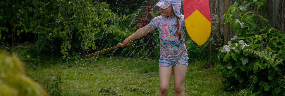 Young girl with decorated shield and sword playing with water sprinkler