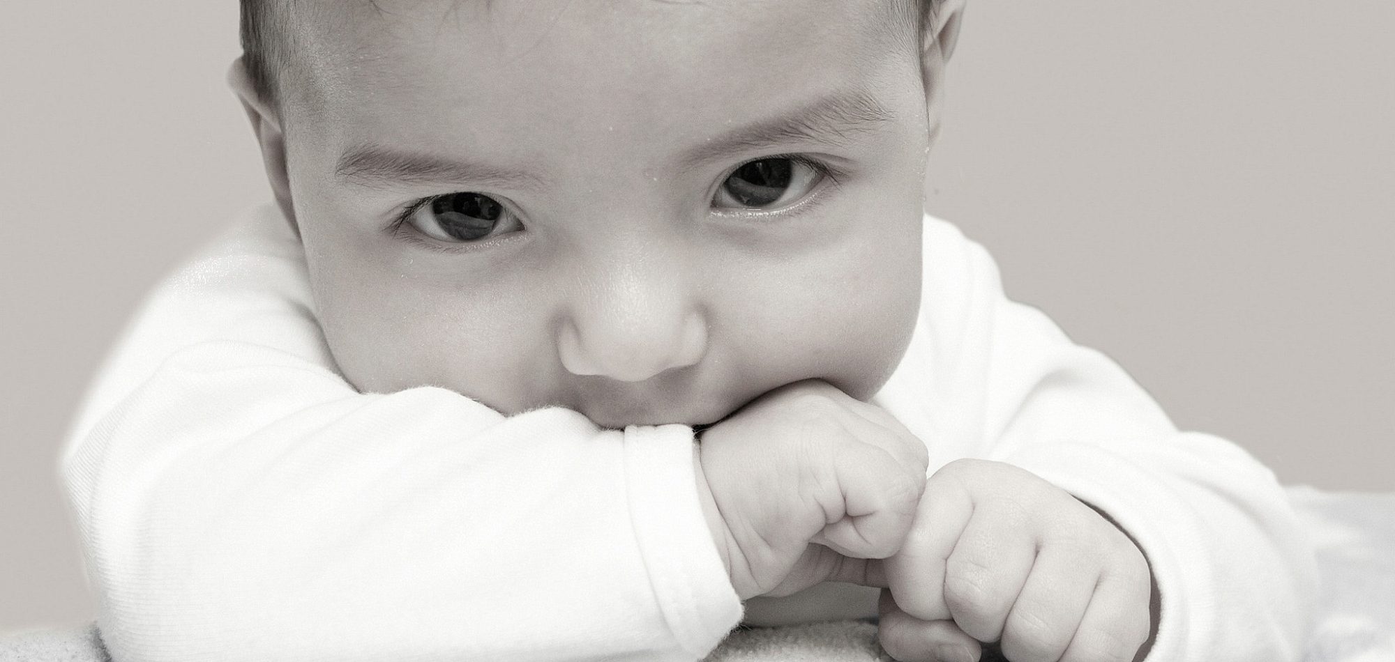 Monochrome portrait of a young baby, resting head on hands looking at camera