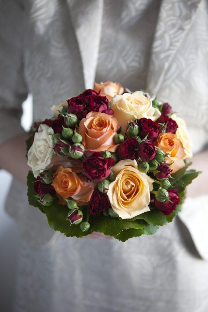Close of bridal bouquet of red, peach and pale yellow roses held by the bride.