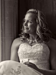 Monochrome image of bride in white dress softly lit by window light.