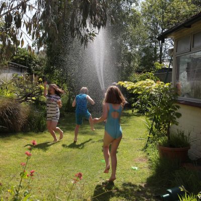 Children playing in a spray of water in a mature garden with lots of plants