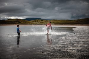 Two young boys standing fully clothed in the waters of a bay splashing each other.